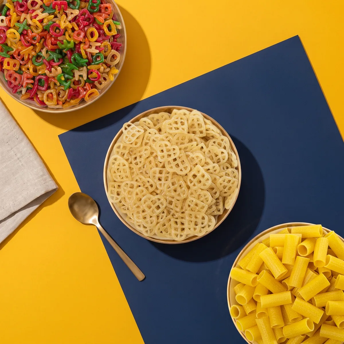 Overhead view of brass bowls of Suvidha Papad ABCD, Dil and 1-inch Pipe on a turmeric and navy table